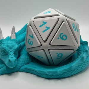 May include: A teal dragon figurine cradles a large, multi-sided die. The die is white with teal numbers. The dragon is detailed with horns and scales, and the die has the numbers 1 through 20. The overall theme is fantasy and gaming.