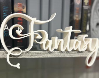 May include: A cream-colored, 3D-printed sign that spells out the word "Fantasy" in a cursive font. The sign is placed on a shelf in front of a blurred background of books. The letters have a whimsical, decorative design.