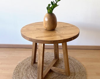 Table ronde Blenom en bois naturel avec pieds en bois croisés. Table d'appoint avec finition rustique idéale pour canapé. Mod. Matapi.