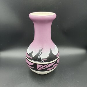 May include: A purple ceramic vase with a black and white design of trees and a bird. The vase has a rounded body and a narrow neck.