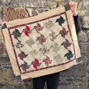 May include: A beige quilt with a patchwork design featuring green, red, and white pinwheels. The quilt is made of various fabrics with floral and geometric patterns.