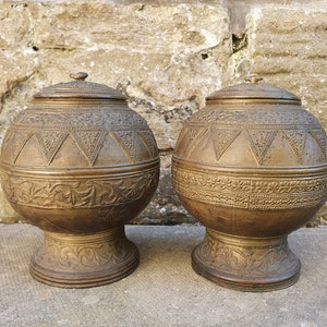 May include: Two antique bronze urns with intricate floral and geometric designs. The urns have a round body and a wide base.