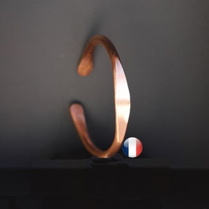 Peut inclure: Un bracelet en cuivre avec une finition martelée. Le bracelet est ouvert et a une forme légèrement incurvée.