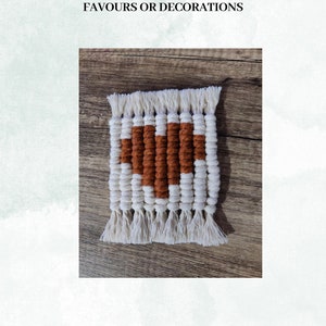 May include: A small, square, woven wall hanging with a brown heart design. The hanging is made with white and brown yarn and has fringe on all sides.