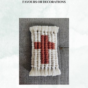 May include: A small, handmade wall hanging in the shape of a cross. The cross is made of white and rust-coloured yarn.