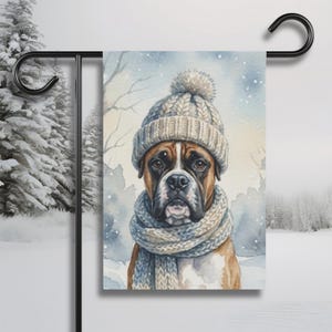 Peut inclure: Un drapeau de jardin avec une peinture à l'aquarelle d'un chien Boxer portant un bonnet et une écharpe en tricot. Le chien est brun et blanc avec un nez noir, sur fond d'hiver enneigé. Le drapeau rectangulaire est suspendu à un poteau en métal noir.