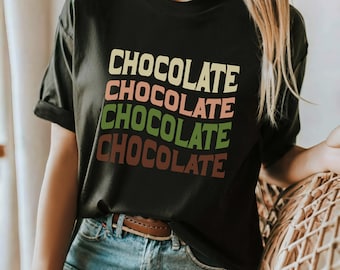 Könnte beinhalten: Schwarzes T-Shirt mit dem Wort "SCHOKOLADE" viermal in einem gestapelten Design wiederholt. Jedes Wort ist in einer anderen Farbe: Pfirsich, Gelb, Grün und Braun.