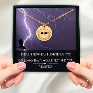 Peut inclure: Un collier en or avec un pendentif rond repr&eacute;sentant une silhouette de dragon noir &agrave; l'int&eacute;rieur d'une couronne. Le pendentif est dans une bo&icirc;te avec un fond violet et un motif d'&eacute;clair. Le texte sur la bo&icirc;te est : "THERE IS NOWHERE IN EXISTENCE YOU COULD GO THAT I WOULD NOT FIND YOU, VIOLENCE."