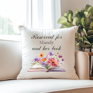 May include: White pillow with the text "Reserved for Mandy and her book" and a watercolor illustration of an open book with colorful flowers.
