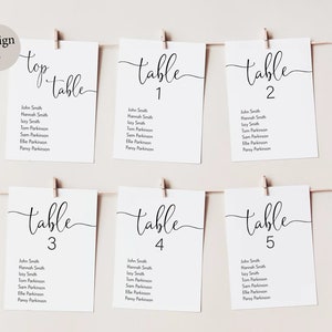 Peut inclure: Cartes blanches avec calligraphie noire listant les num&eacute;ros de table et les noms des invit&eacute;s. Les cartes sont accroch&eacute;es &agrave; une ficelle avec des pinces &agrave; linge. La carte du haut indique "top table".