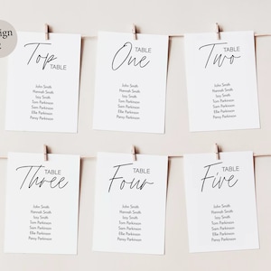 Peut inclure: Cartes blanches avec calligraphie noire pour une r&eacute;ception de mariage. Les cartes sont &eacute;tiquet&eacute;es "Top Table", "Table One", "Table Two", "Table Three", "Table Four", et "Table Five". Chaque carte liste les noms des invit&eacute;s assign&eacute;s &agrave; cette table.