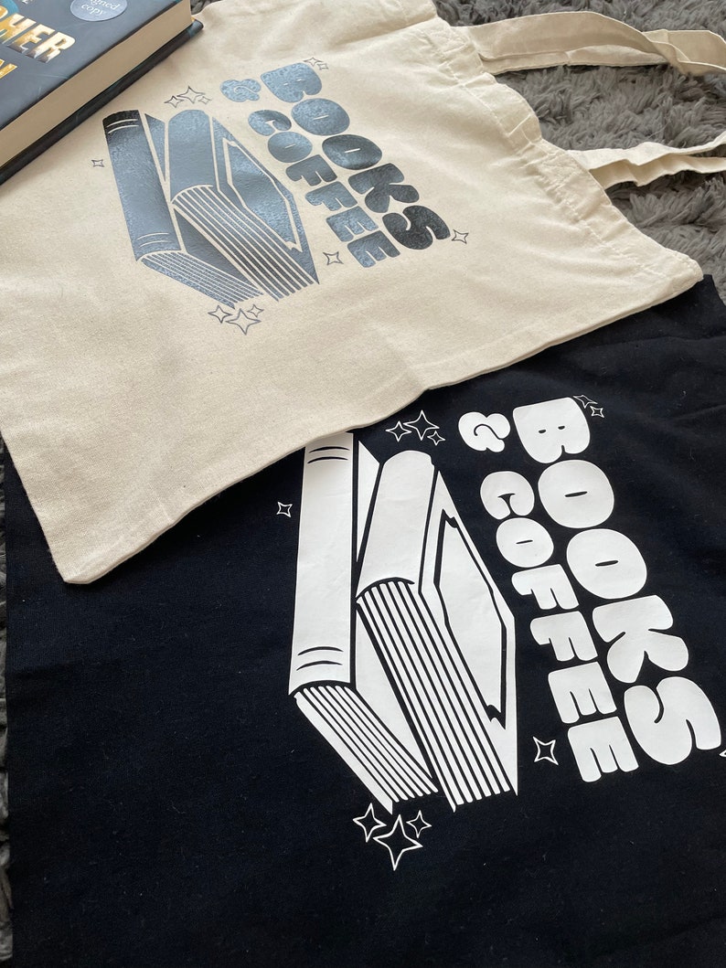 以下が含まれることがあります： 「Books & Coffee」という文字が印刷されたトートバッグが2つあります。1つは黒で、もう1つはベージュです。両方のバッグには、スタイリッシュな本の積み重ねのイラストが描かれています。