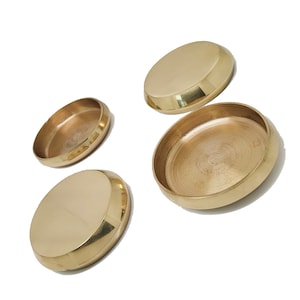 May include: Four gold-coloured metal bowls of varying sizes. The bowls are round and have a smooth, shiny finish.