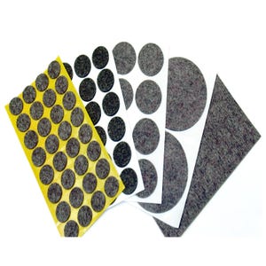 May include: A selection of grey felt furniture pads in various shapes and sizes. The pads are arranged on yellow and white backing sheets, with some individual pads and a larger felt sheet visible. The pads are designed to protect floors from scratches.