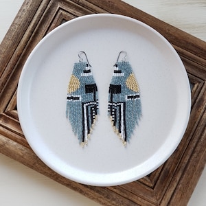May include: A pair of blue, black, and gold beaded earrings with a geometric pattern. The earrings are hanging from silver hooks.