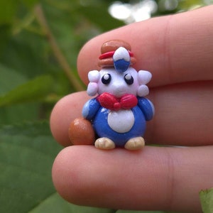 May include: A small blue and white figurine of a penguin wearing a brown hat and a red bow tie. The penguin is holding a brown egg in its right flipper.