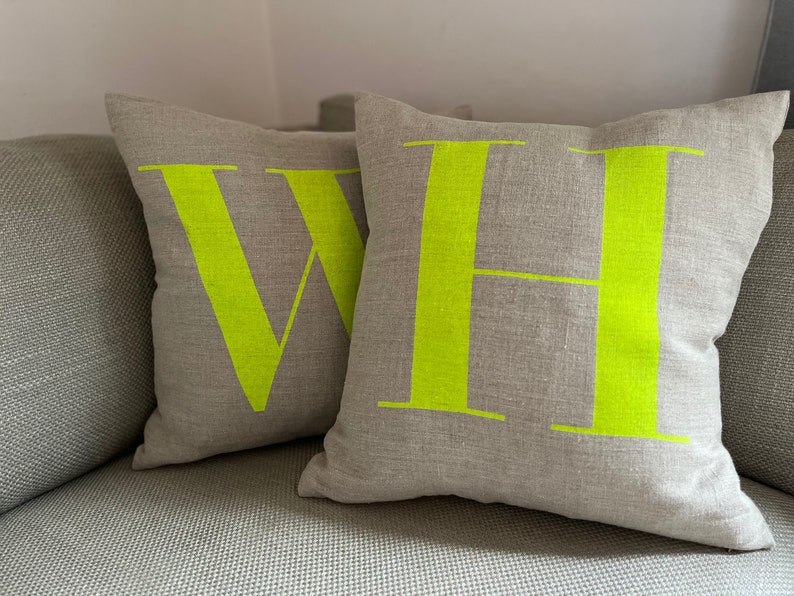 May include: Two throw pillows with a linen fabric cover. The pillows have the letters "W" and "H" printed in bright neon yellow.