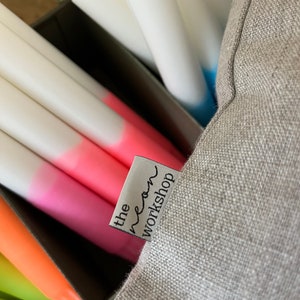 May include: A grey linen cushion with a white label that says "the neon workshop" in black text.