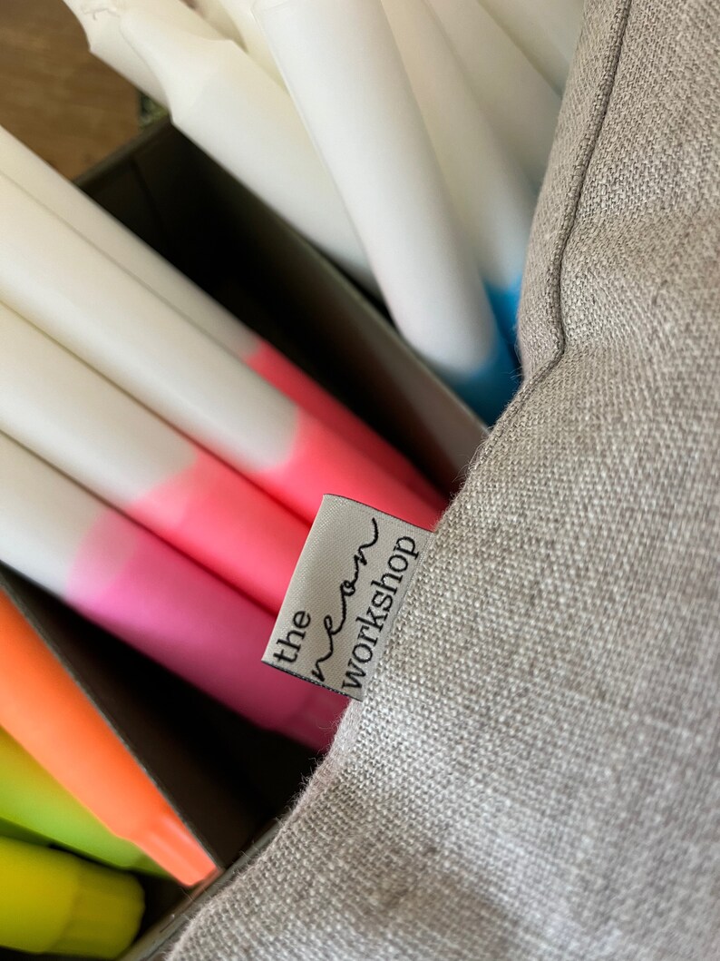 May include: A grey linen cushion with a white label that says "the neon workshop" in black text.