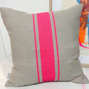May include: A grey linen cushion with two wide pink stripes down the centre. The cushion is on a white surface.