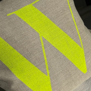 May include: A beige linen cushion with a bright yellow letter W printed on the front.