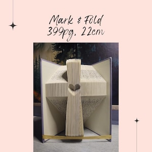 Könnte beinhalten: Ein Buch, das zu einem Kreuz gefaltet ist, mit einem ausgeschnittenen Herzen in der Mitte. Das Buch hat 399 Seiten und ist 22 cm hoch. Mark & Fold steht oben im Bild.