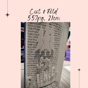 Puede incluir: Un libro con páginas cortadas y dobladas para crear una escena de bosque con las palabras "Love Silence". El libro mide 21 cm de alto y tiene 557 páginas. El texto "Cut & Fold" está escrito en la parte superior.