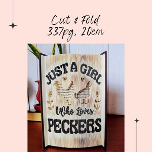 May include: A book art sculpture made from a book with the text "Just a girl who loves peckers" and two chickens cut out of the pages. The sculpture is 20 cm tall and made from 337 pages.