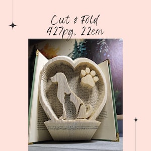 Può includere: Una scultura di arte libraria di un cane e un'impronta di zampa all'interno di una forma di cuore, realizzata dalle pagine di un libro. Il libro è aperto e la scultura è alta 22 cm ed è realizzata con 427 pagine.