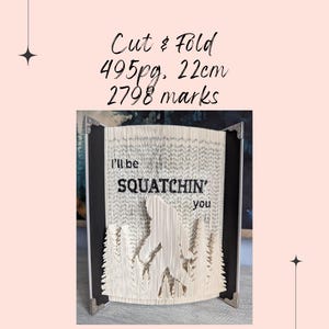 May include: A cut and folded book with the text "I'll be Squatchin' you" carved into the pages. The book is 22cm tall and has 495 pages. The book art features a Bigfoot silhouette in a forest setting.