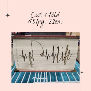 May include: A book with a cut-out design of a person fishing with the words "Life" and a heartbeat graphic. The book is 451 pages and 22 cm long.