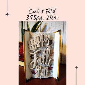 May include: A book art sculpture with the words "Happy Fall Y'all" created by folding the pages of a book. The sculpture is 21 cm tall and made from 345 pages.