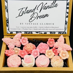 Puede incluir: Una caja de 85 g de fundentes de cera de soja Island Vanilla Dream con un diseño floral. Los fundentes están hechos a mano en Maryland y con ingredientes de origen ético. La caja está decorada con un patrón floral y el texto "Island Vanilla Dream" y "By Vintage Glamour".
