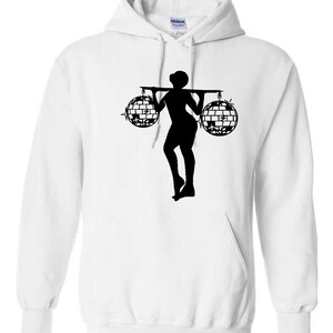 Puede incluir: Sudadera con capucha blanca con una silueta negra de una persona que lleva dos bolas de discoteca en una pértiga.
