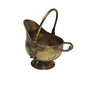 May include: A vintage brass sugar scuttle with a handle and a small side handle. The scuttle has a curved shape and sits on a small pedestal base. Decorative lion head accents are visible on the side.