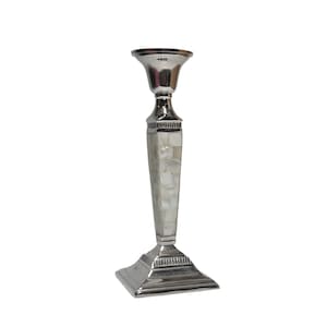 May include: A silver candlestick with a square base and a flared top. The central column is decorated with a mosaic of white, rectangular pieces. The candlestick is designed to hold a single candle and has a classic, elegant appearance.