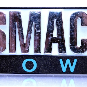 May include: A black and blue sign with the words "SMACK DOWN!" in silver letters. The letters are raised and have a textured surface.