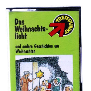 May include: A green cassette tape with a red arrow and the text "Das Weihnachts-licht und andere Geschichten um Weihnachten" and "Herausgegeben von Rolf Krenzer". The cassette tape features a cartoon illustration of children singing carols to an elderly woman.