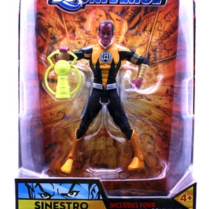 Op de afbeelding: Een geel en zwart Sinestro-actiefiguur uit de DC Universe Classics-lijn. De figuur houdt een gele kracht ring vast en is verpakt in een plastic blisterverpakking met een gele en zwarte achtergrond. De verpakking bevat de tekst "Sinestro Classics Wave 3 Figure 1" en "Includes your Collect & Connect Figure Piece".
