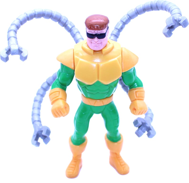 May include: A plastic action figure of Doctor Octopus, a comic book villain. The figure is primarily green and yellow, with four articulated, gray mechanical arms extending from its back. The figure wears black sunglasses and has a brown head.