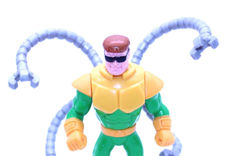 May include: A Dr. Octopus action figure. The figure is primarily green and yellow, with four articulated, light blue mechanical arms extending from its back. The character wears black sunglasses and has a brown hair.