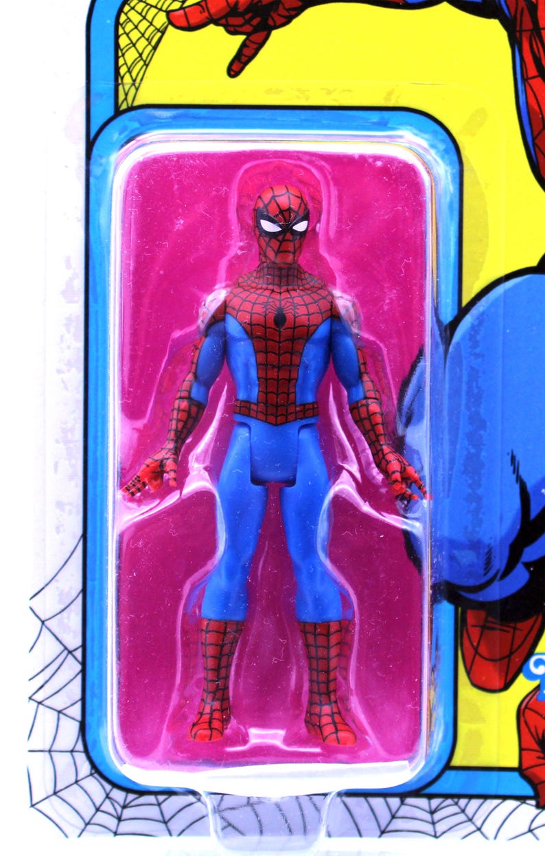 Pu&ograve; includere: Una action figure di Spider-Man rossa e blu in una confezione blister di plastica. La figura &egrave; in posa con le braccia distese e le gambe unite. La figura &egrave; su uno sfondo rosa.