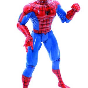 May include: A red and blue plastic action figure of Spider-Man. The figure has a web design on the chest and legs. The figure is posed with one arm raised and the other arm bent at the elbow.