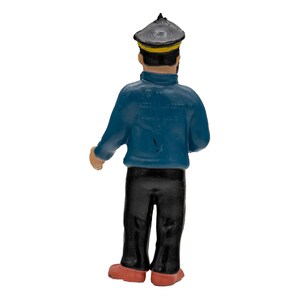 May include: A figurine of a sailor from the back. The sailor is wearing a dark blue jacket, black pants, a black hat with a yellow band, and red shoes. The figurine is standing.