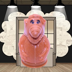 Puede incluir: Una figura vintage de Alf, de color naranja claro. El personaje alienígena coleccionable tiene ojos azules y un rostro detallado. La figura está frente a un telón de fondo temático de cómic, iluminado por focos.