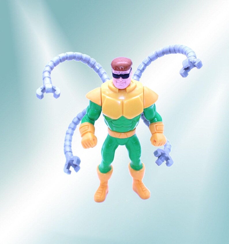 May include: A Dr. Octopus action figure. The figure is wearing a yellow and green outfit with four articulated, light purple mechanical arms. The figure has a brown head and black sunglasses. The figure is standing.
