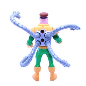 May include: A Dr. Octopus action figure, viewed from the back, with a yellow and green torso, green legs, and orange boots. The figure has a brown head and four articulated, gray mechanical arms extending from its back.