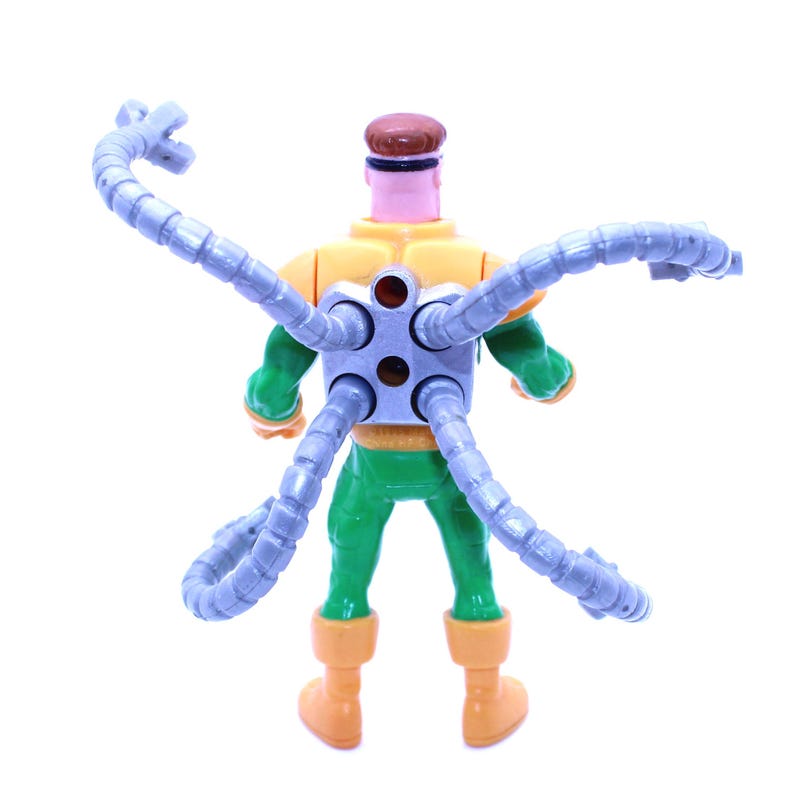 May include: A Dr. Octopus action figure, viewed from the back, with a yellow and green torso, green legs, and orange boots. The figure has a brown head and four articulated, gray mechanical arms extending from its back.