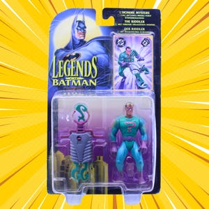Könnte beinhalten: Ein Legends of Batman Actionfiguren-Set mit dem Riddler. Die Figur befindet sich in einer transparenten Kunststoffverpackung mit einer Batman-Grafik und Text in mehreren Sprachen. Die Riddler-Figur trägt ein grün-violettes Kostüm.