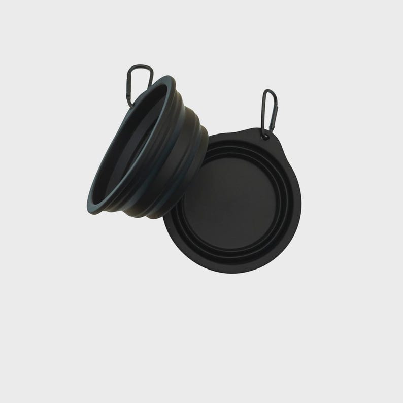 May include: Two black collapsible bowls made of flexible material, each featuring a circular rim and a flat base. Both bowls include a small integrated tab with a metal carabiner attached, allowing for easy hanging or attachment to other items.
